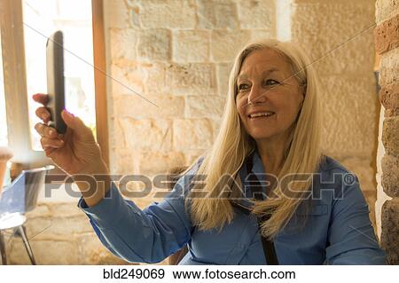 Stock Photo - Older Caucasian woman posing for cell phone selfie. Fotosearch