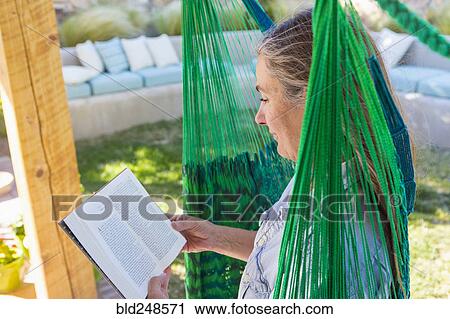 Stock Image - Older Caucasian woman reading book in green hammock. Fotosearch