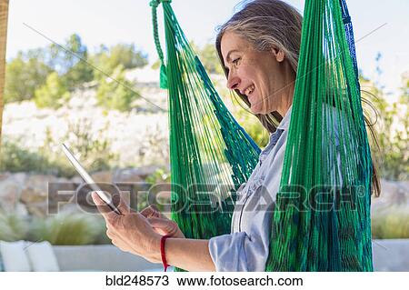 Older Caucasian woman reading digital tablet in green hammock View Large Photo Image Stock Image - Older Caucasian woman reading digital tablet in green hammock. Fotosearch