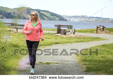 Picture - Older Caucasian woman running on path in park. Fotosearch