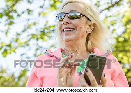 Picture - Older Caucasian woman texting on cell phone outdoors. Fotosearch