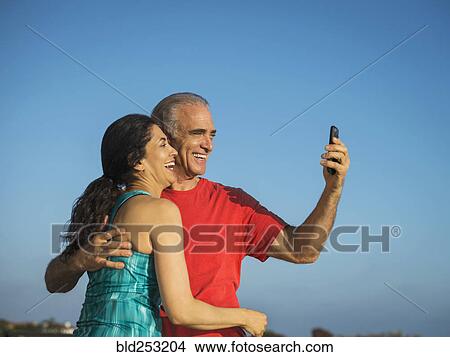 Picture - Older couple laughing and posing for cell phone selfie. Fotosearch
