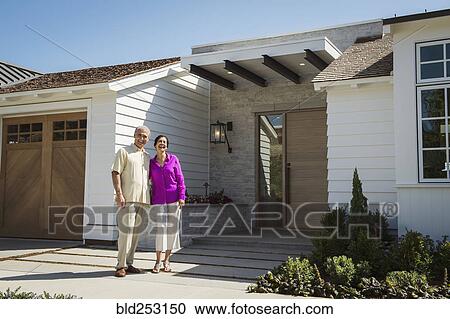 Stock Image - Older couple posing near driveway of house. Fotosearch