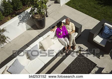 Stock Image - Older couple relaxing on modern backyard patio. Fotosearch