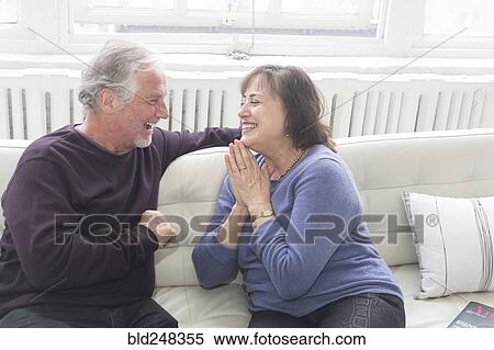 Stock Photography - Older couple sitting on sofa and laughing. Fotosearch