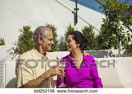 Stock Photo - Older couple toasting on modern backyard patio. Fotosearch