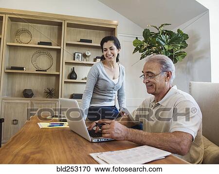 Stock Image - Older couple using laptop in home office. Fotosearch