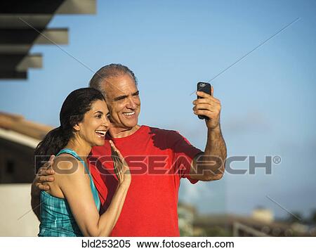 Stock Photography - Older couple waving and posing for cell phone selfie. Fotosearch