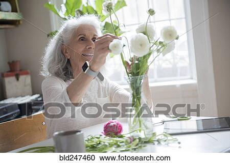 Stock Image - Older woman arranging flowers. Fotosearch
