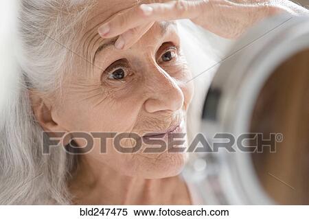 Older woman checking eye wrinkles in mirror View Large Photo Image Stock Photography - Older woman checking eye wrinkles in mirror. Fotosearch