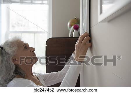 Older woman hanging artwork on wall View Large Photo Image Stock Image - Older woman hanging artwork on wall. Fotosearch
