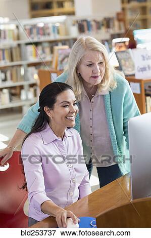 Older woman helping woman using computer in library View Large Photo Image Stock Photo - Older woman helping woman using computer in library. Fotosearch