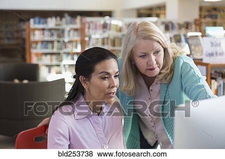 Older woman helping woman using computer in library View Large Photo Image Stock Photo - Older woman helping woman using computer in library. Fotosearch