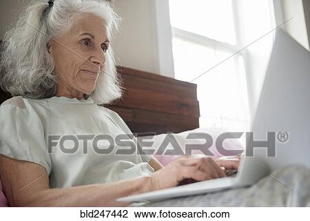 Older woman laying in bed using laptop View Large Photo Image Stock Image - Older woman laying in bed using laptop. Fotosearch