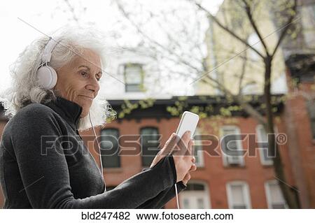 Older woman listening to cell phone with headphones in city View Large Photo Image Stock Image - Older woman listening to cell phone with headphones in city. Fotosearch