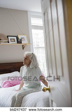 Older woman sitting on bed beyond doorway View Large Photo Image Stock Photo - Older woman sitting on bed beyond doorway. Fotosearch