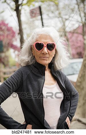 Stock Image - Older woman wearing heart-shape sunglasses. Fotosearch