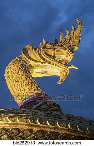 Stock Image - Ornate golden snake statue under cloudy sky. Fotosearch