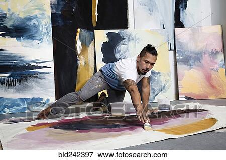 Stock Photo - Pacific Islander artist kneeling on floor painting on canvas. Fotosearch