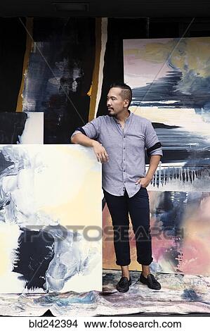 Picture - Pacific Islander artist leaning on paintings. Fotosearch