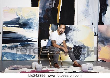 Stock Photograph - Pacific Islander artist sitting with paintings. Fotosearch