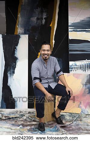 Stock Photography - Pacific Islander artist sitting with paintings. Fotosearch