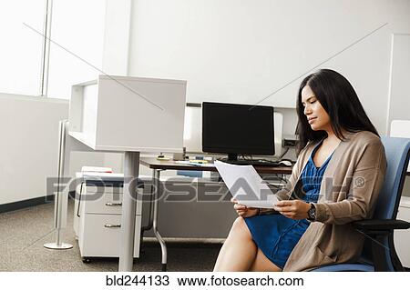 Stock Image - Pacific Islander woman reading paperwork in office. Fotosearch