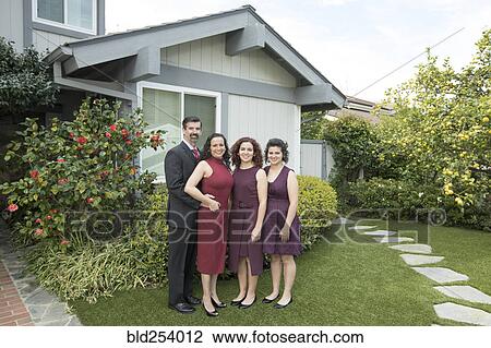 Stock Image - Parents and daughters posing near house. Fotosearch