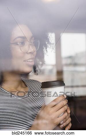 Stock Photograph - Pensive African American woman drinking coffee behind window. Fotosearch