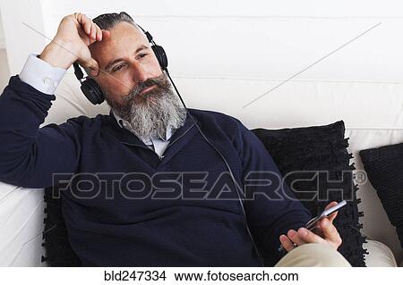 Pensive Caucasian man listening to cell phone with headphones View Large Photo Image Picture - Pensive Caucasian man listening to cell phone with headphones. Fotosearch