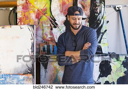 Stock Image - Pensive Caucasian man standing near paintings. Fotosearch