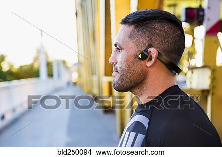 Picture - Pensive Caucasian man wearing modern headphones on bridge. Fotosearch