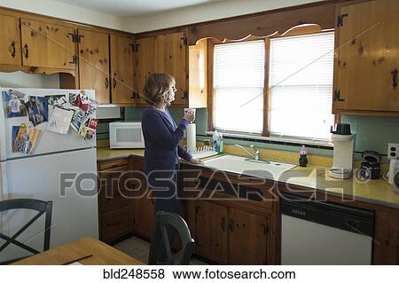 Pensive Caucasian woman drinking coffee in kitchen View Large Photo Image Stock Photo - Pensive Caucasian woman drinking coffee in kitchen. Fotosearch
