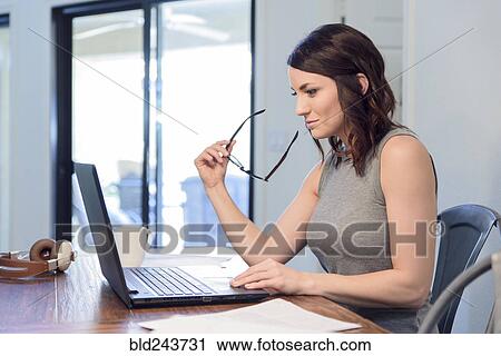 Stock Image - Pensive Caucasian woman holding eyeglasses using laptop. Fotosearch
