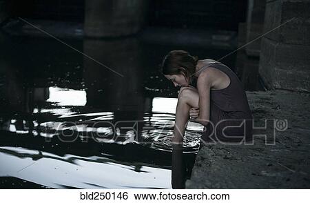 Pensive Caucasian woman sitting at edge of water View Large Photo Image Stock Photograph - Pensive Caucasian woman sitting at edge of water. Fotosearch