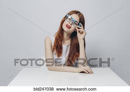 Stock Photo - Pensive Caucasian woman sitting at table wearing blue eyeglasses. Fotosearch