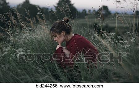 Stock Photograph - Pensive Caucasian woman sitting in tall grass. Fotosearch