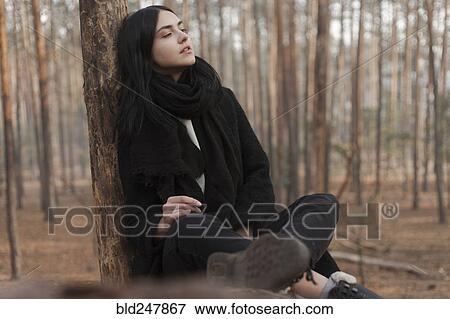 Stock Photo - Pensive Caucasian woman sitting on log in forest. Fotosearch