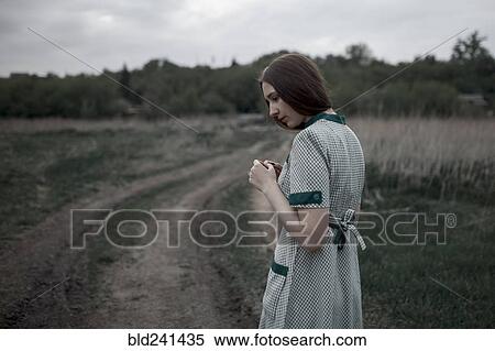 Stock Photography - Pensive Caucasian woman standing near dirt road. Fotosearch