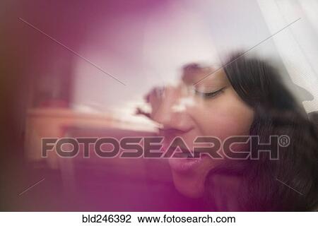 Stock Image - Pensive Hispanic woman behind window. Fotosearch