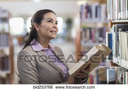 Stock Photograph - Pensive Hispanic woman holding book in library. Fotosearch