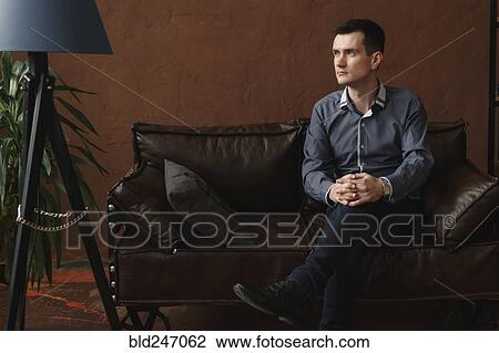 Stock Image - Pensive Middle Eastern man sitting on sofa. Fotosearch