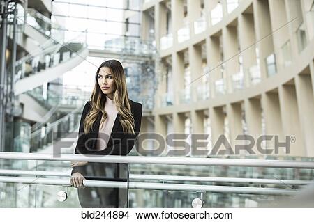 Picture - Pensive Mixed Race businesswoman leaning on railing in lobby. Fotosearch