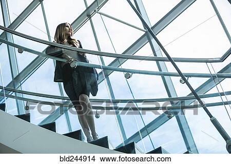 Pensive Mixed Race businesswoman standing on staircase View Large Photo Image Picture - Pensive Mixed Race businesswoman standing on staircase. Fotosearch