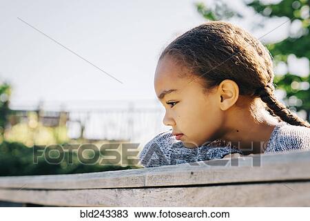 Stock Image - Pensive Mixed Race girl leaning on wooden railing. Fotosearch