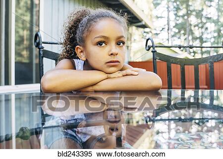 Stock Photography - Pensive Mixed Race girl leaning on glass table. Fotosearch