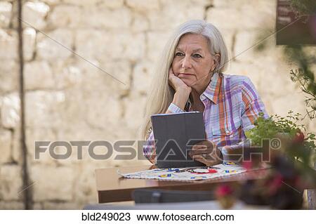 Stock Image - Pensive older Caucasian woman using digital tablet. Fotosearch