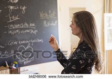 Stock Photograph - Pensive teacher holding chalk near blackboard. Fotosearch