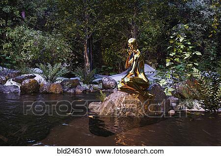 Stock Image - Pensive woman robot sitting on rock at river. Fotosearch