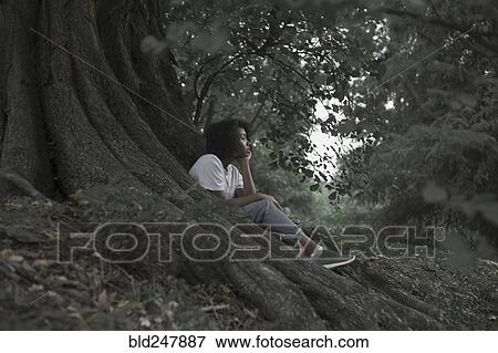 Pensive woman sitting on tree roots in forest View Large Photo Image Stock Photo - Pensive woman sitting on tree roots in forest. Fotosearch